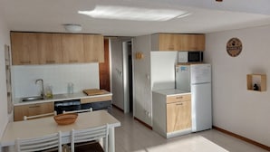 Una cocina compacta con armarios de madera, una encimera blanca, un microondas, un refrigerador y un lavamanos.