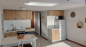 Una cocina compacta con armarios de madera, una encimera blanca, un microondas, un refrigerador y un lavamanos.