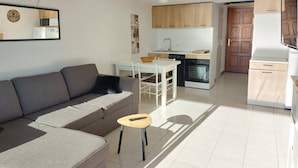 Una sala de estar moderna con un sofá gris, una mesita redonda y una cocina con armarios de madera, un microondas y un lavavajillas.