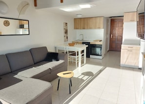 Una sala de estar moderna con un sofá gris, una mesita redonda y una cocina con armarios de madera, un microondas y un lavavajillas.