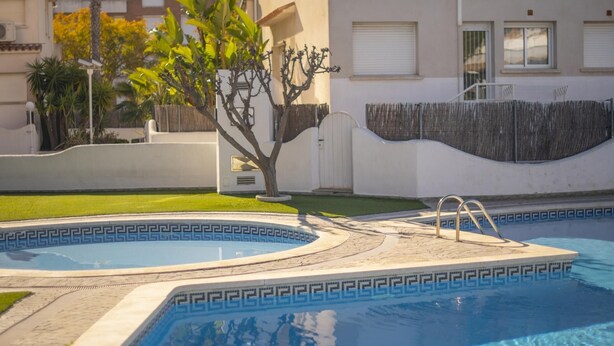 Una piscina con un diseño geométrico de baldosas, rodeada por una zona pavimentada y un pequeño árbol.