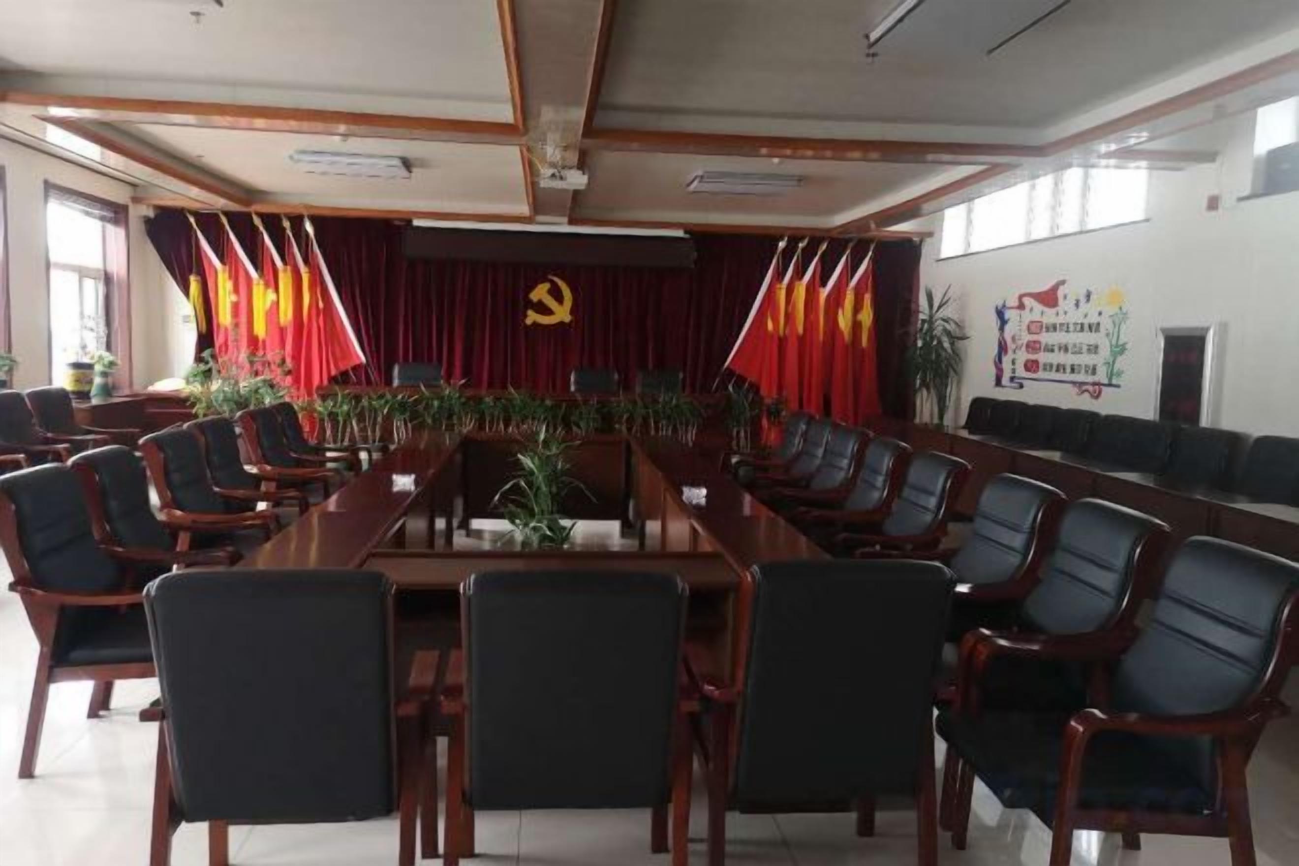 Een congreszaal met een lange tafel en stoelen, een spreekgestalte en een achtergrond met vlaggen en een hamer en sikkel embleem.