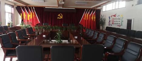 Ein Konferenzraum mit einem langen Tisch, Stühlen, einem Rednerpult und einem Hintergrund mit Flaggen und dem Emblem eines Hämmerchens und Sensels.