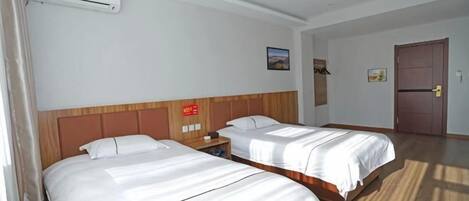 A hotel room with two beds, a wooden headboard, a nightstand, a wall-mounted air conditioner, and a door.