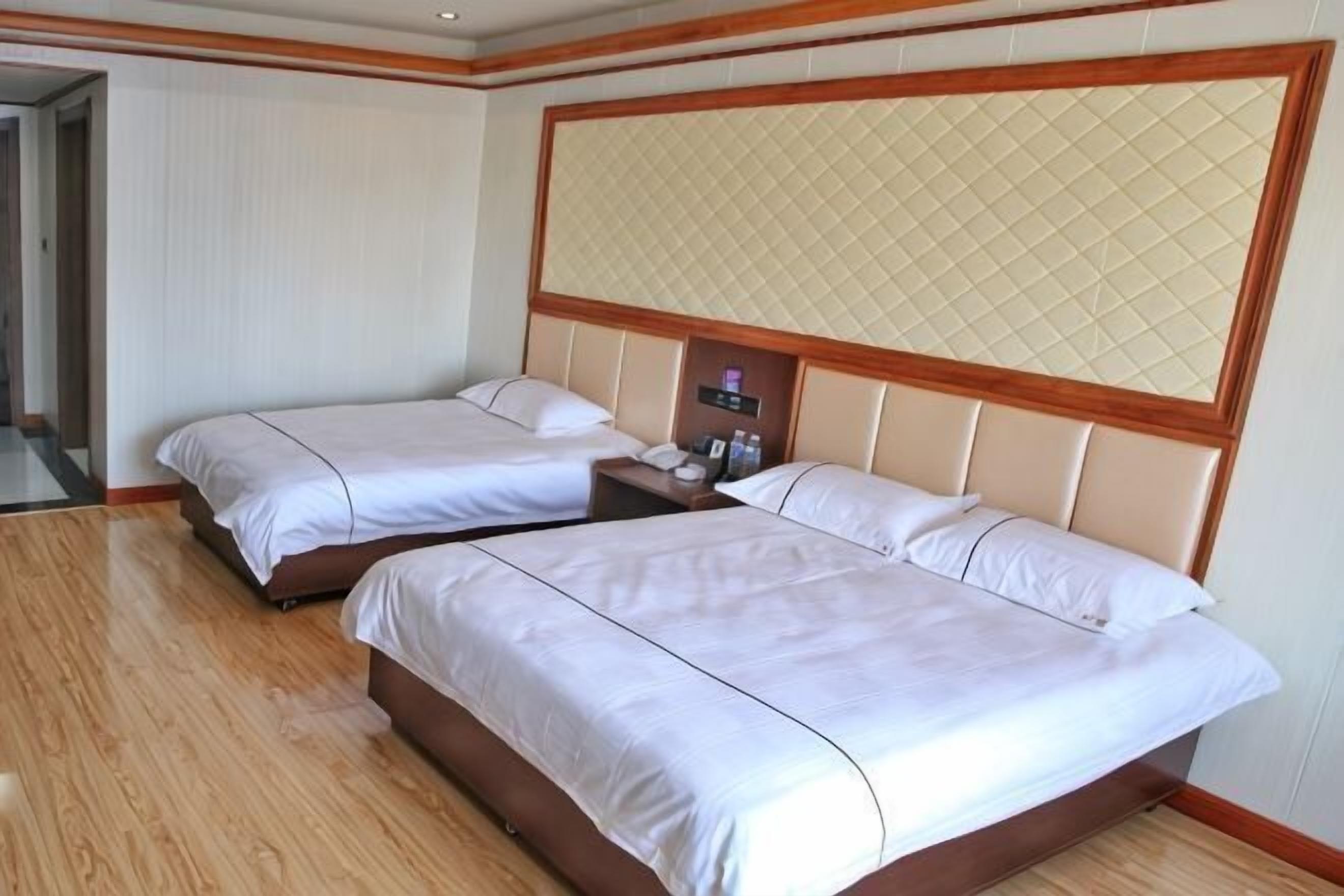 Habitación de hotel con dos camas, un cabecero de madera, una mesita de noche y una mesita auxiliar.
