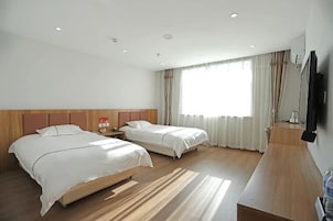 Une chambre d’hôtel avec deux lits, une tête de lit en bois, un téléviseur à écran plat et une grande fenêtre avec des rideaux.