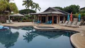 Una piscina con lettini e ombrelloni, circondata da palme e un'area porticata.