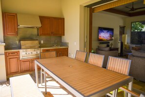 Une cuisine moderne avec des meubles en bois, un four encastré et un coin repas comprenant une longue table et des chaises.