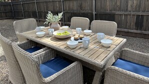 En uteservering med flätade stolar och ett träbord, redo för en måltid.