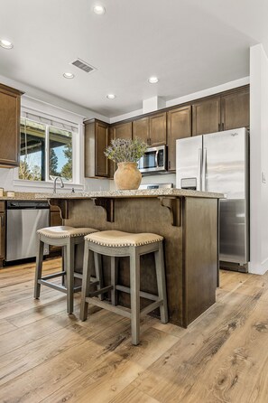 A kitchen with wooden cabinets, a stainless steel refrigerator, a microwave, and a sink. There are two stools under the island. - Hiking, Skiiing and. Holidays in the Mountains! (Flagstaff)