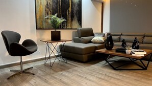 A modern living room with a sectional sofa, a black chair, a coffee table, and a large abstract painting on the wall. - Modern Prestigious 24-hour Electricity 5 min from the Beach! (Ghazir)