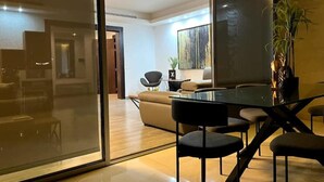 A modern living room with a glass partition, a dining area with a glass table and black chairs, and a large window with a view of the interior. - Modern Prestigious 24-hour Electricity 5 min from the Beach! (Ghazir)