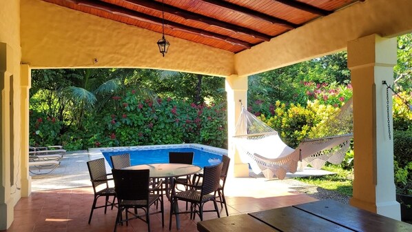 Relax in a serene outdoor space with a pool, wicker chairs, and a hammock, surrounded by lush greenery.