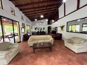 Relax in this spacious living area with a high ceiling, featuring a central coffee table and comfortable seating for relaxation and dining.