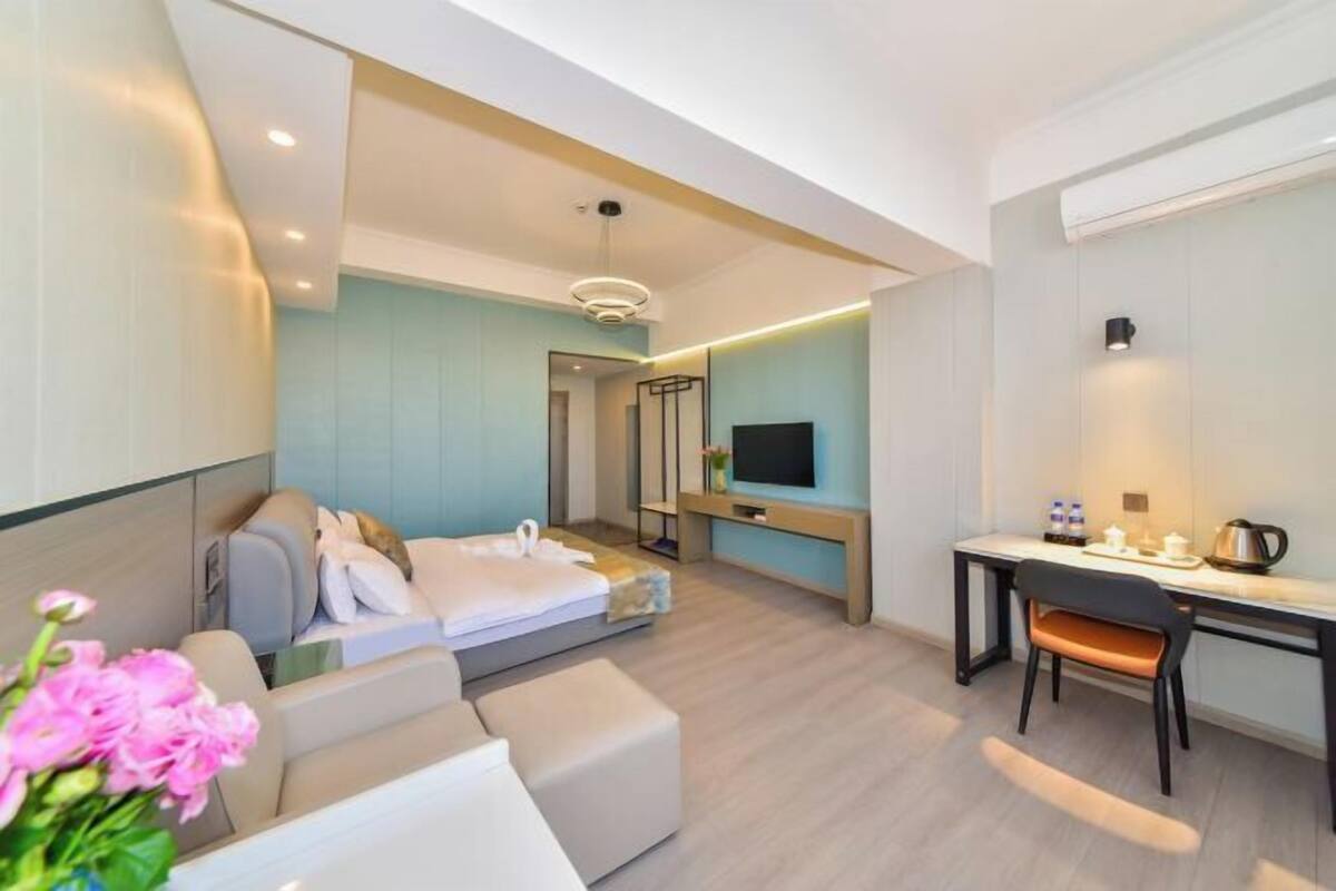 A modern hotel room with a bed, a desk, a chair, a TV, and a small kitchenette.