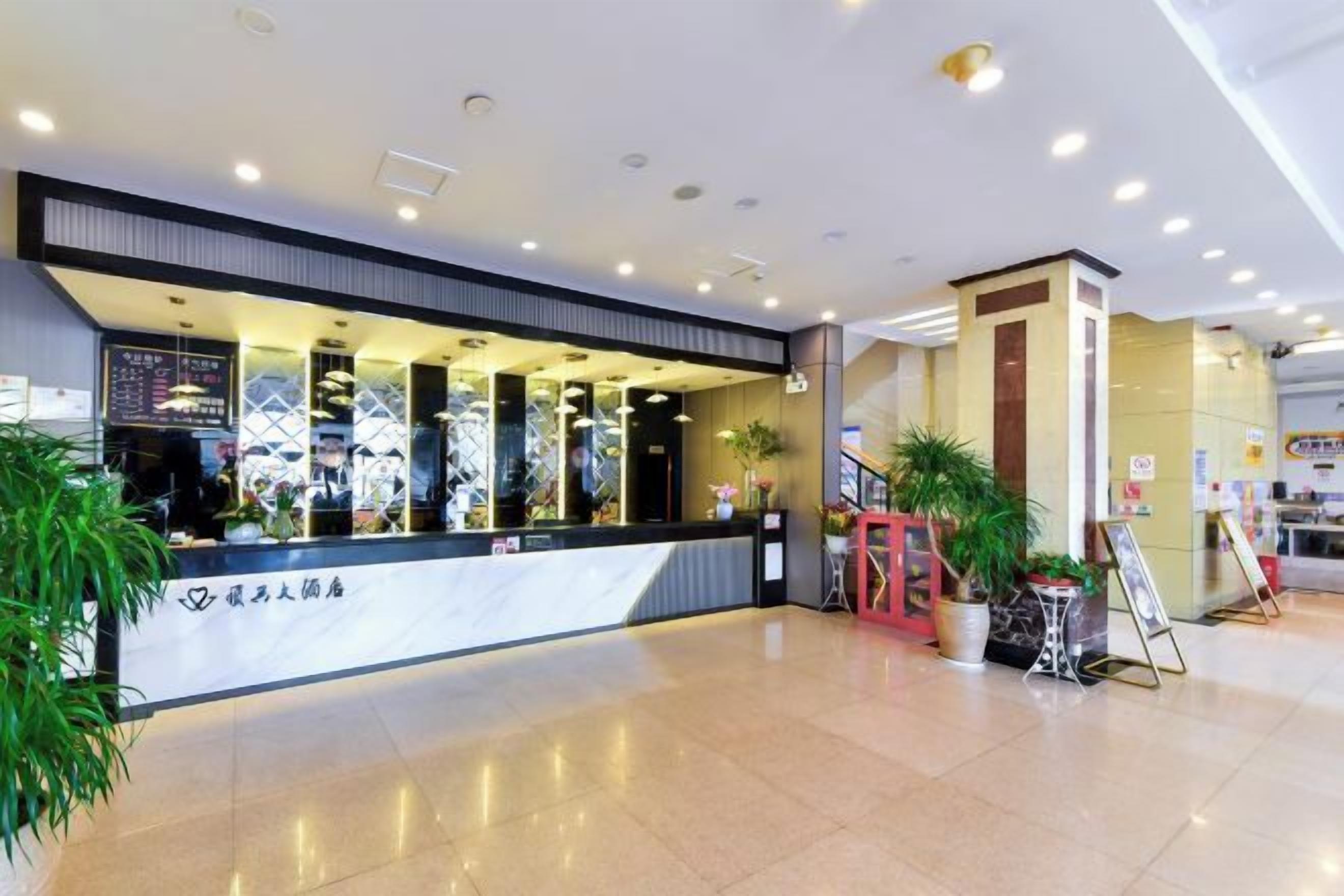 Zona de recepción de un hotel con mostrador de mármol, plantas en macetas y una escalera.