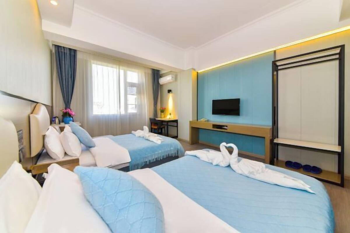 A hotel room with two beds, a TV, a desk, and a window with curtains.