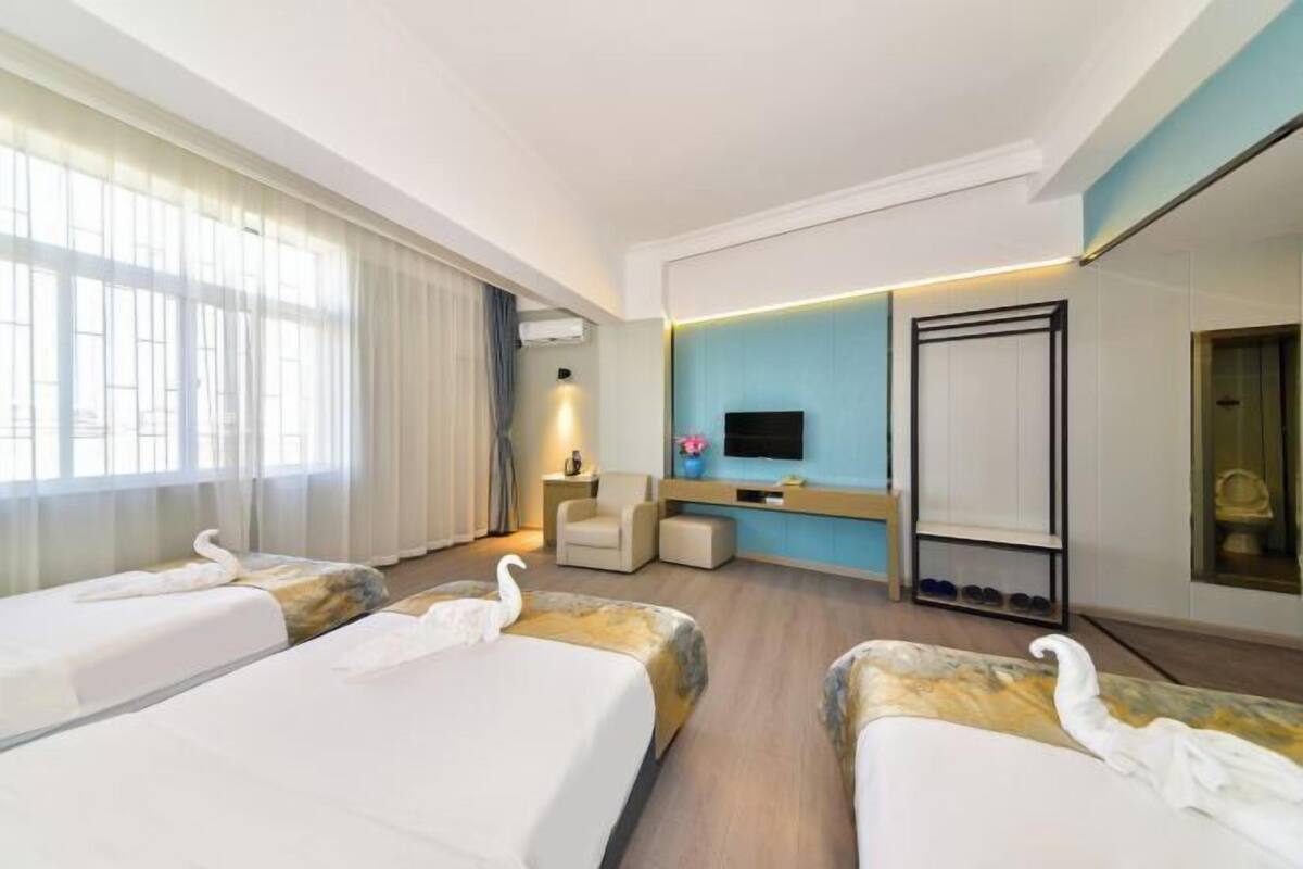 A hotel room with three beds, a TV, a desk, and a mirror.