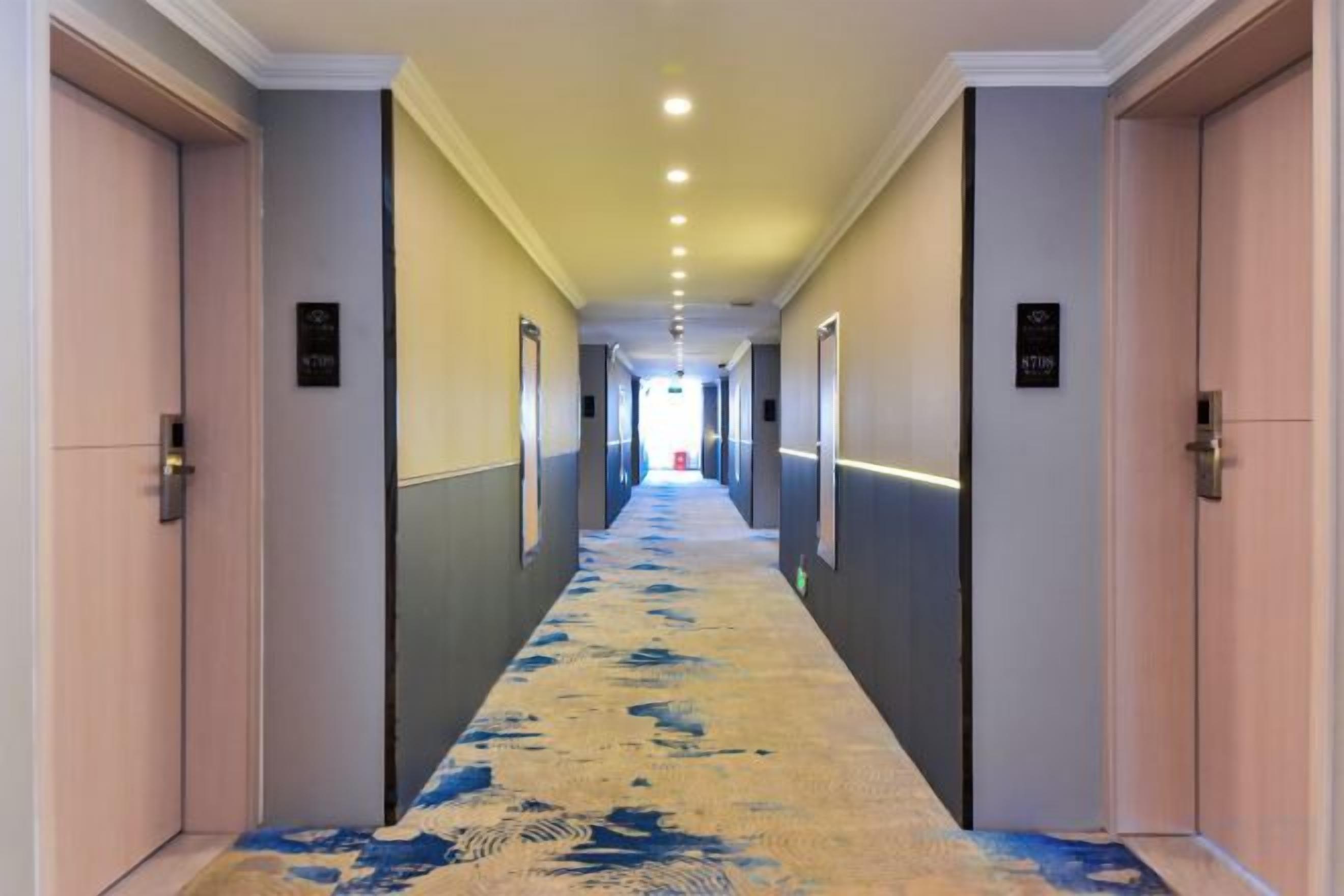 Un pasillo de hotel con puertas a ambos lados, piso alfombrado e iluminación empotrada en el techo.