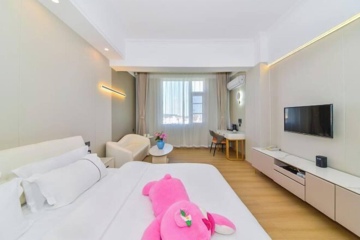 A hotel room with a bed, a desk, a chair, a TV, and a window with curtains.