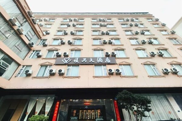 A multi-story hotel building with air conditioning units, a sign with Chinese characters, and a storefront with a digital display. - Shun Xing Hotel (Dali City)