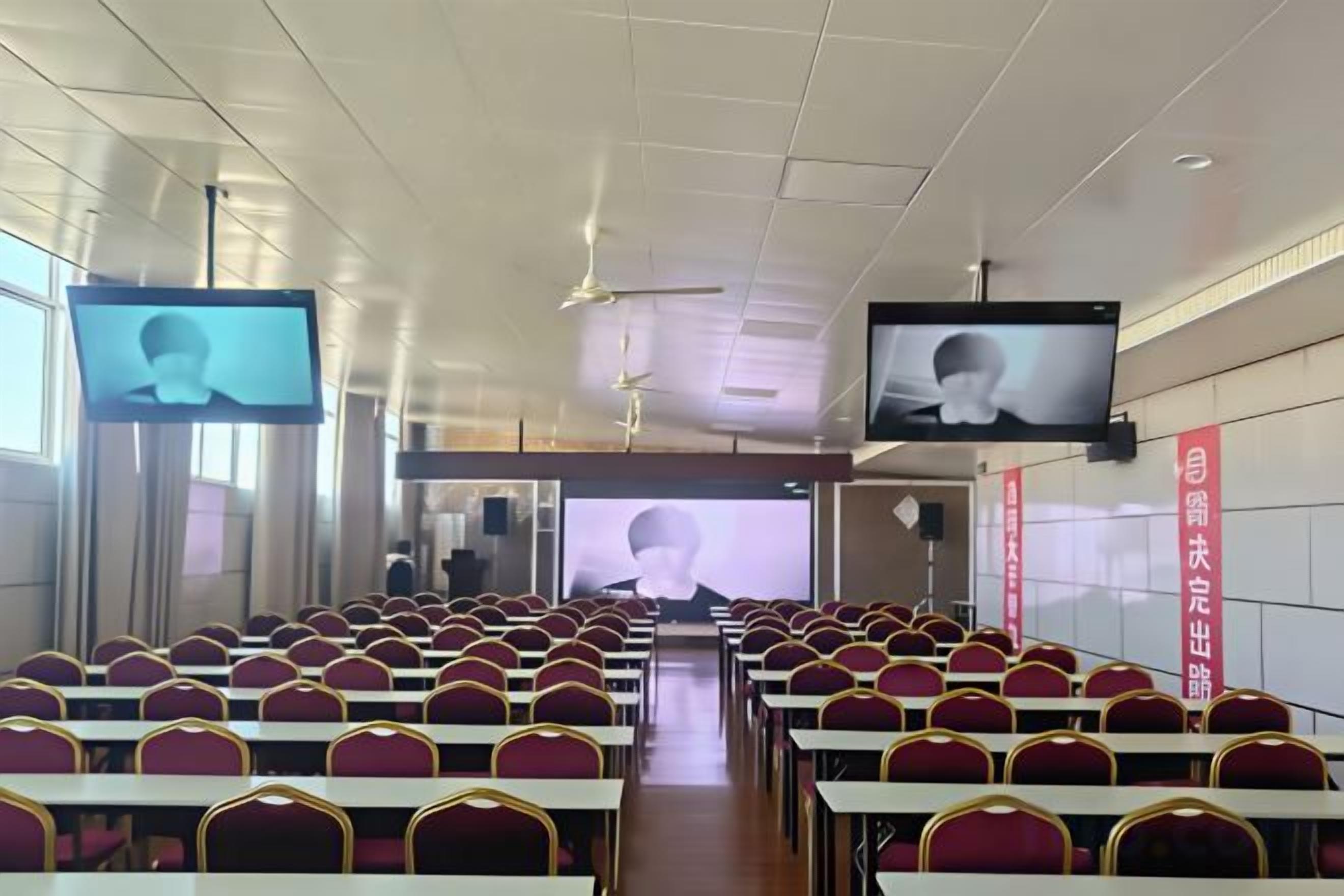 A conference room with rows of chairs, a stage, and two large screens.
