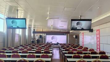 A conference room with rows of chairs, a stage, and two large screens.