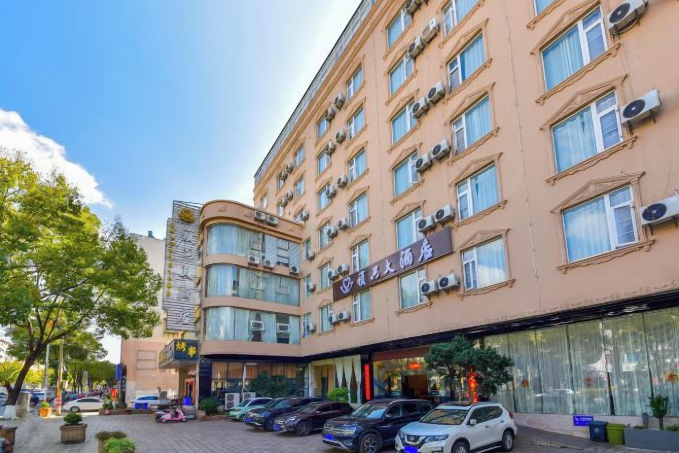 A multi-story hotel with a modern facade, large windows, and a parking area with several cars.