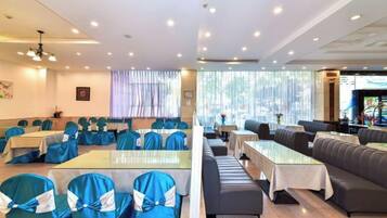 Uma área de refeições de hotel com mesas, cadeiras, um balcão comprido e um espaço de estar com sofás.