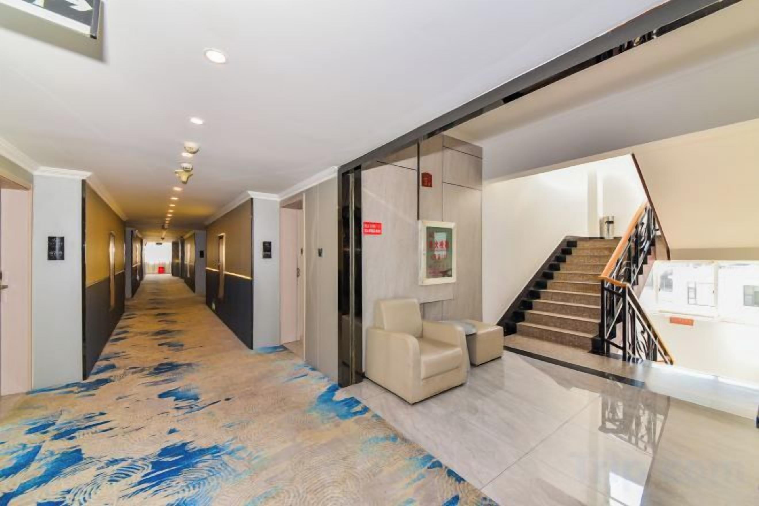 A hotel corridor with a carpeted floor, a staircase, and a seating area.
