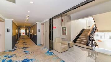 A hotel corridor with a carpeted floor, a staircase, and a seating area.