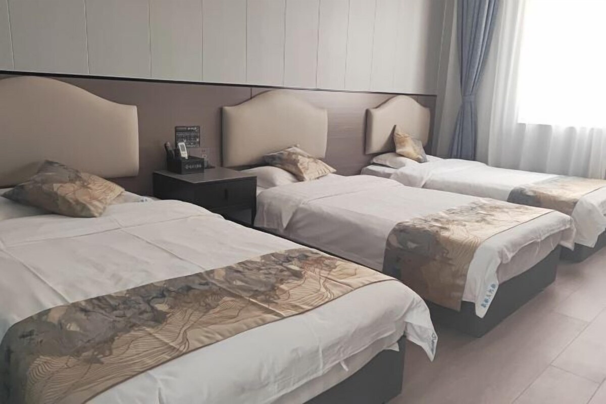 Ein Hotelzimmer mit drei Betten, jedes mit Kopfteil und Nachttisch.