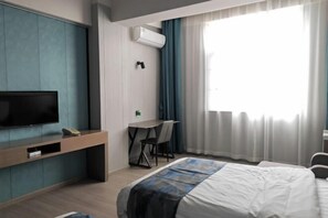 A hotel room with a bed, a TV, a desk with a chair, and a window with curtains. - Shun Xing Hotel (Dali City)