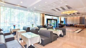 Un vestíbulo de hotel con zonas de estar, mesas y una recepción.