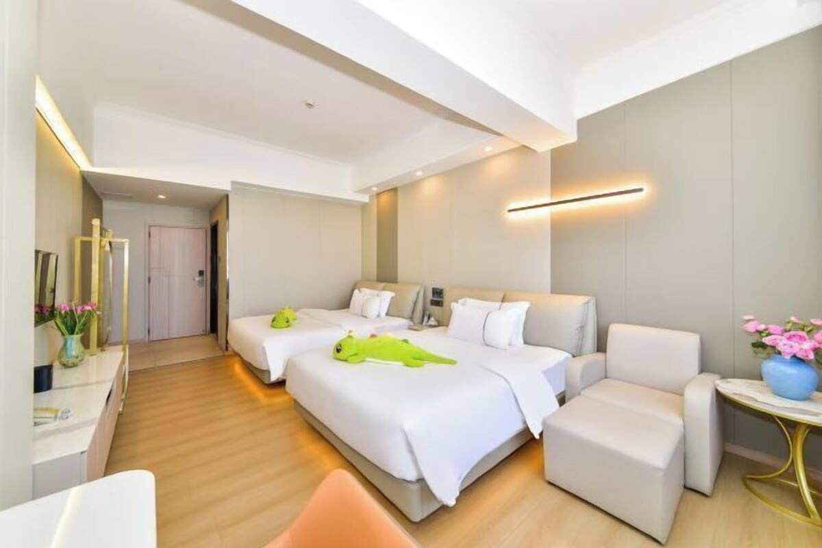 A hotel room with two beds, a desk, a chair, and a small table with flowers.