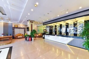 A modern hotel lobby with a reception desk, seating area, and decorative plants. - Shun Xing Hotel (Dali City)