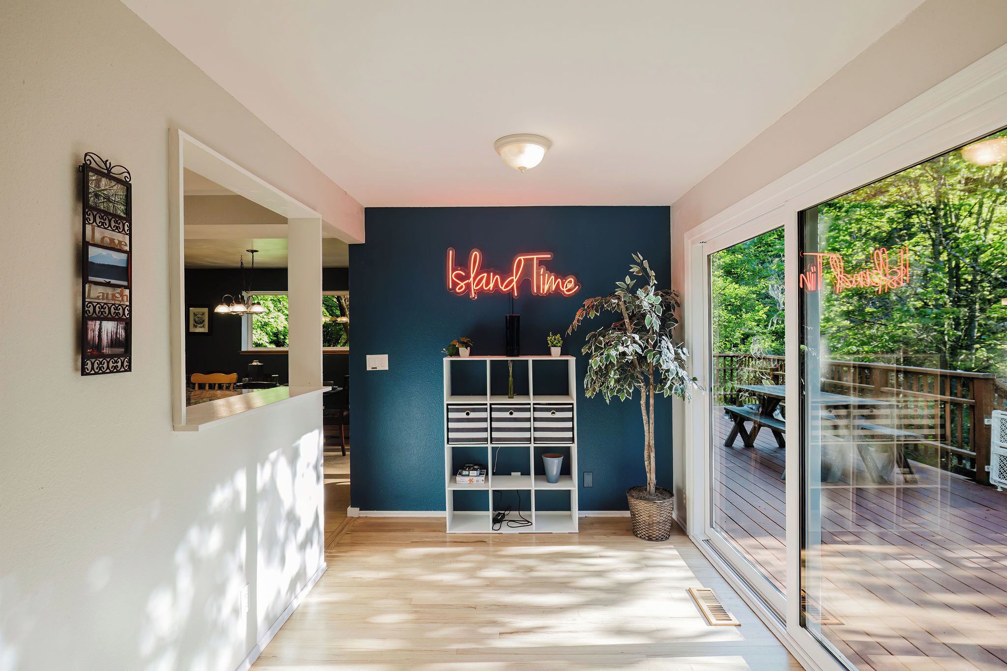 Ein modernes Interieur mit einem Neon-Schild mit der Aufschrift "Island Time", einem Holzboden, einem weißen Regal und Blick auf eine Außenterrasse.