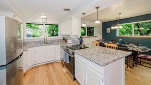 A modern kitchen with white cabinets, granite countertops, and a central island. - Hot Tub / Home Theater / Private Acre / Walk to Beach / Family and Dog friendly (Bainbridge Island)