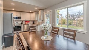 A modern kitchen with white cabinets, stainless steel appliances, and a dining area with a wooden table and chairs. - Walk to Downtown [] Game Room [] Private Fenced Yard (Fruita)