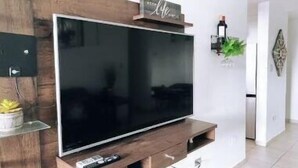 A modern living room with a large flat-screen TV mounted on a wooden wall unit. - Penthouse in San Juan, 2 Beds, Comfortable A/C (San Juan)