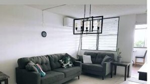 A modern living room with a grey sofa, a smaller armchair, a coffee table, and a hanging light fixture. - Penthouse in San Juan, 2 Beds, Comfortable A/C (San Juan)