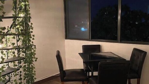 A dining area with a table and chairs, a window with a view of the night sky, and a wall-mounted shelf with green plants and lights. - Penthouse in San Juan, 2 Beds, Comfortable A/C (San Juan)