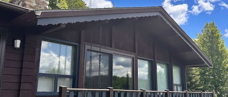 A cabin with a porch, large windows, and a stone chimney.