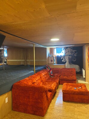 A room with a wooden ceiling, a large mural on the wall, a sofa, a chair, and a small ottoman.