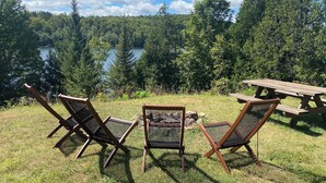 Ein Picknickplatz mit zwei Stühlen und einem Tisch, mit Blick auf einen See, der von dichtem Wald umgeben ist.