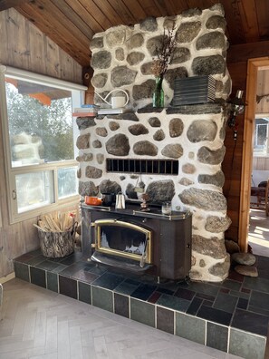 A stone fireplace with a black metal stove, a window, and a stone wall.