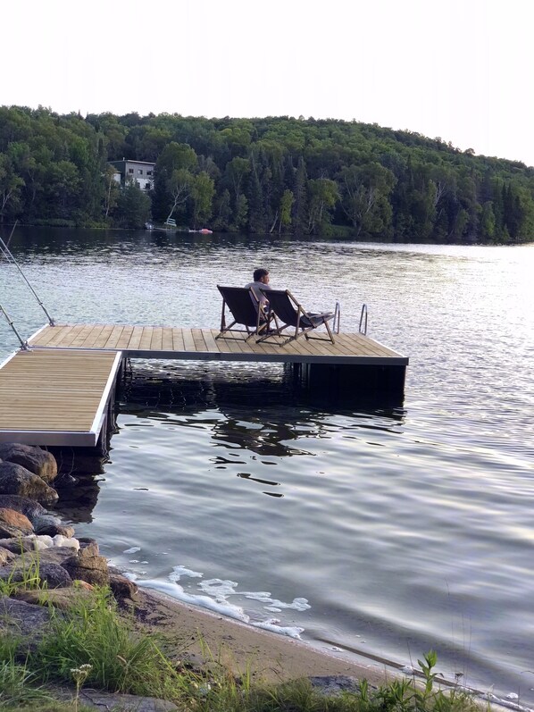 A wooden dock extending into calm water with a person sitting on a chair.