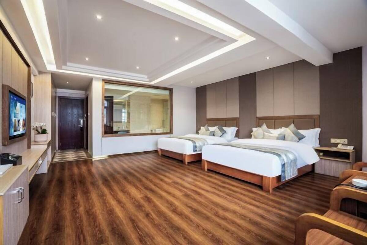 A modern hotel room with two beds, a large mirror, a TV, and a wooden floor.