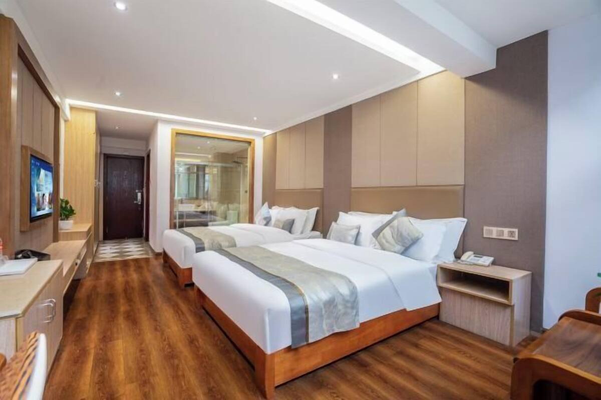 A hotel room with two beds, a desk, a chair, a nightstand, and a mirror.