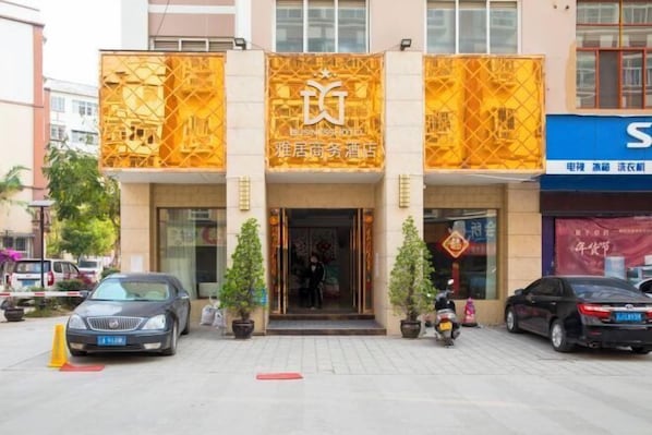 A hotel entrance with a golden facade, a signboard with Chinese characters, and a few parked cars. - Yaju Hotel (Lancang)